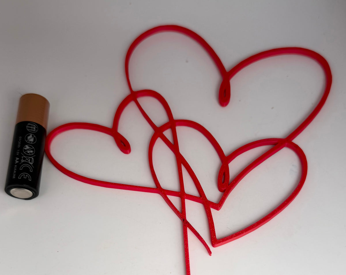 Intertwined hearts cake topper next to an AA battery for scale