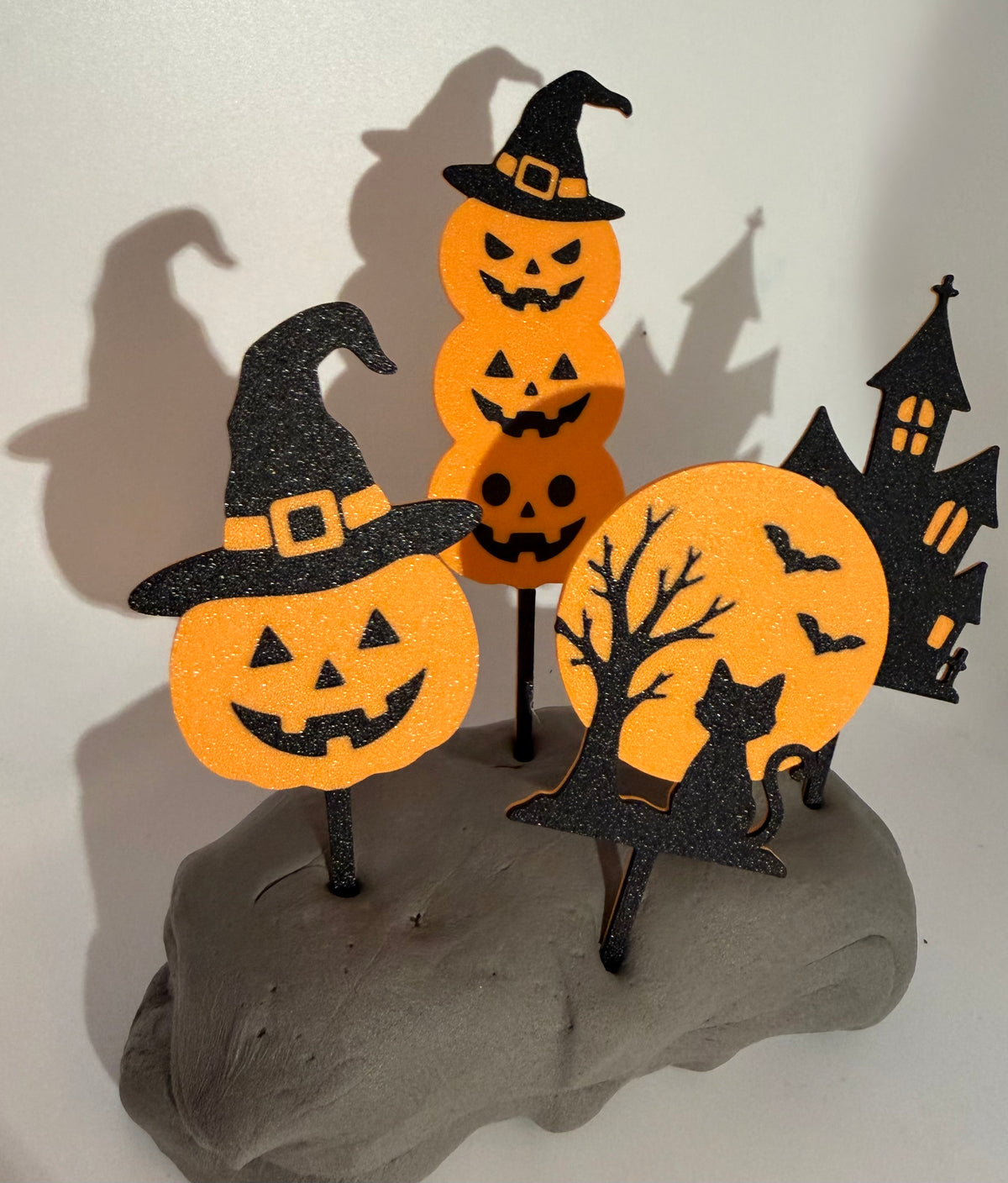 Four orange and black Halloween cake toppers: pumpkins, haunted house, moon and witch hat