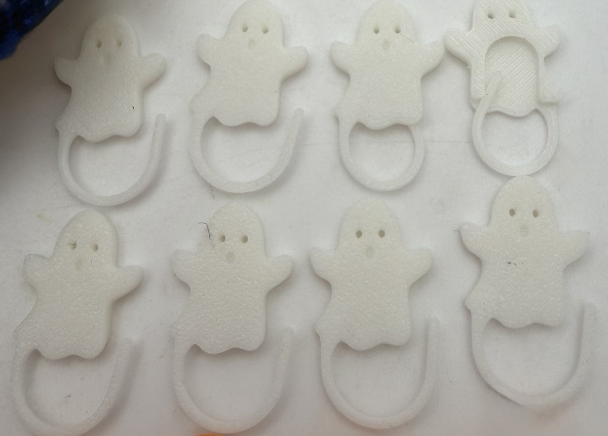 White ghost Halloween stitch markers laid out in rows