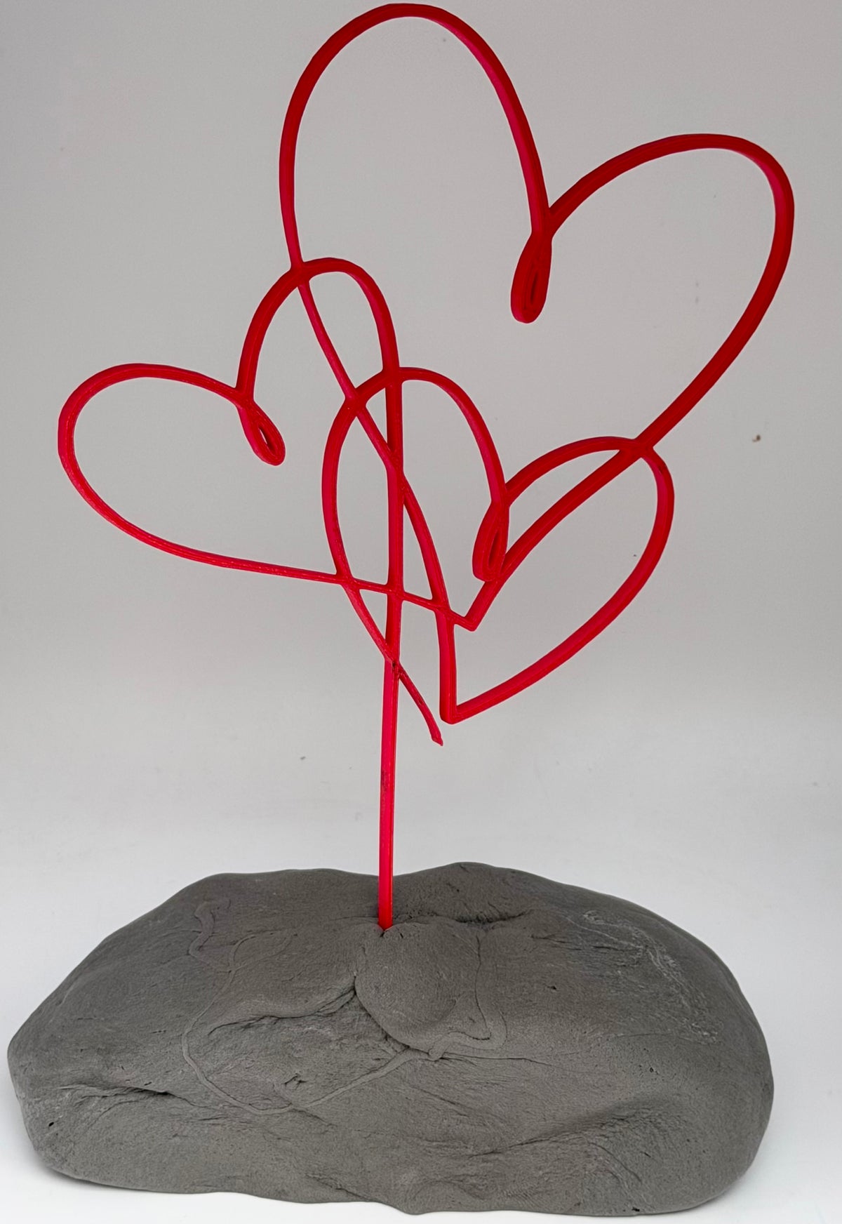 Red intertwined hearts cake topper standing in grey clay