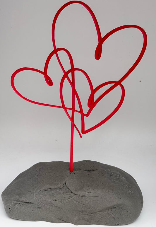 Red intertwined hearts cake topper standing in grey clay