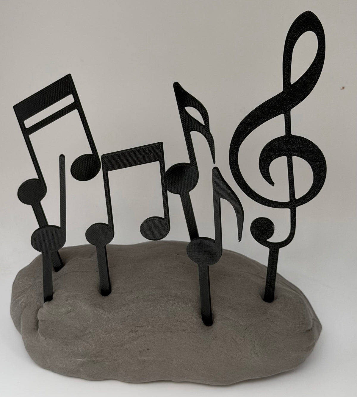 Black music notes and treble clef cake toppers standing in grey clay