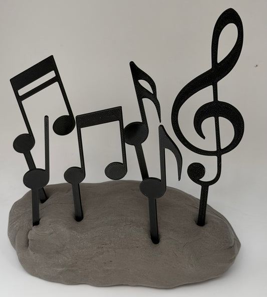 Black music notes and treble clef cake toppers standing in grey clay