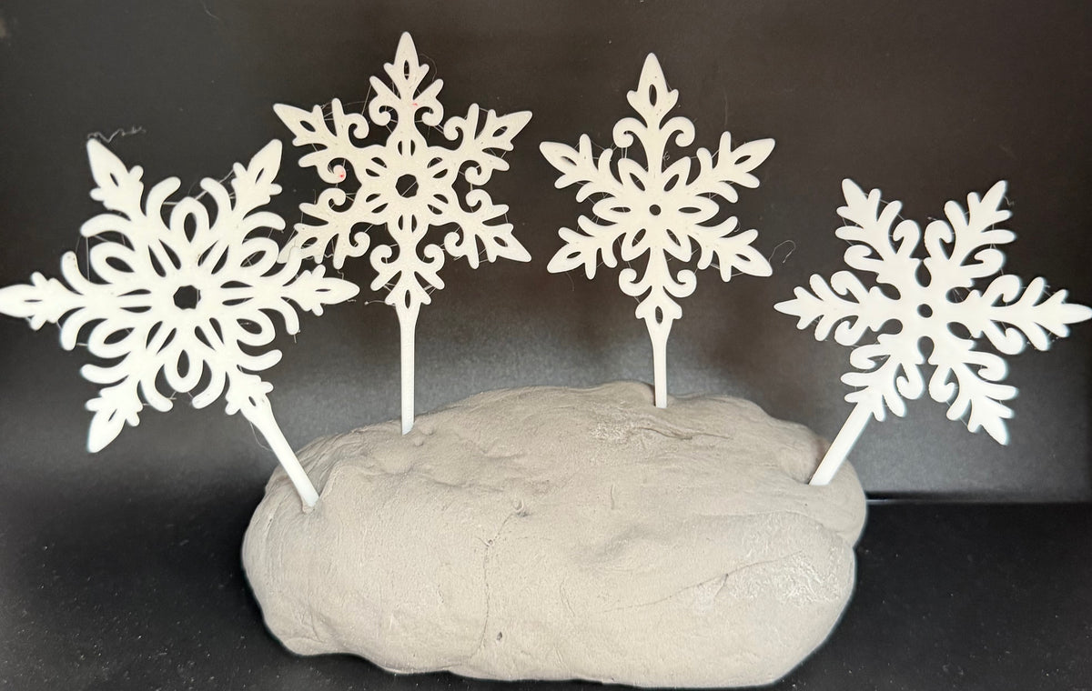 Four white filigree snowflake cake toppers standing in grey clay